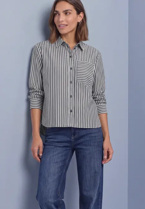 Femme portant une chemise rayée noir et blanc et un jean bleu devant un fond clair.