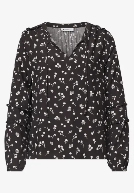 Schwarze Bluse mit weißen Blumenmuster, langen Ärmeln und V-Ausschnitt.