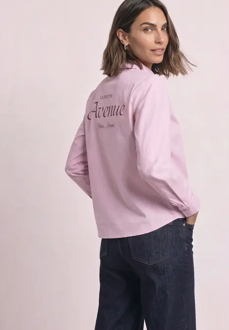 Frau in rosa Langarmshirt und dunkler Jeans, dreht sich, blickt über die Schulter.