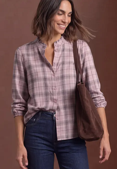 Lächelnde Frau in karierter Bluse, Jeans und brauner Umhängetasche.