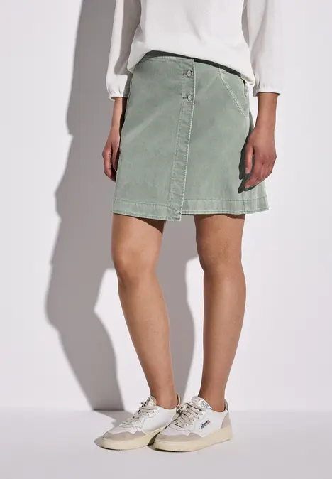 Frau mit mintgrünem Rock, weißem Oberteil und Sneakers.