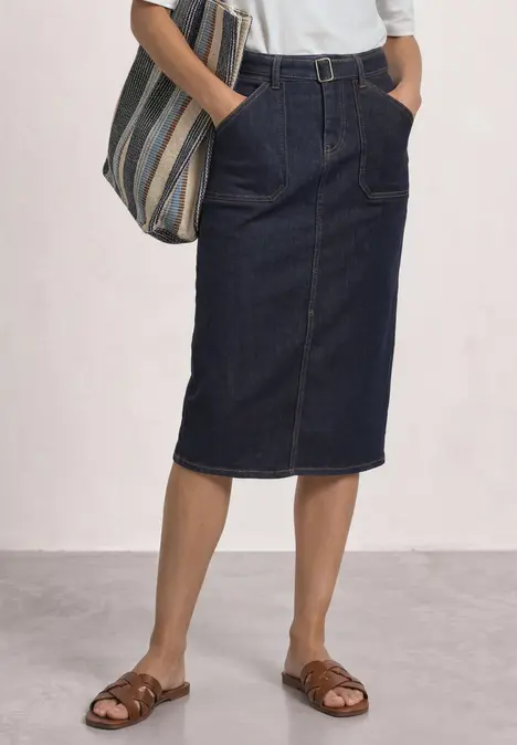 Dame trägt knielangen dunklen Jeansrock, weißes Oberteil, gestreifte Tasche und braune Sandalen.