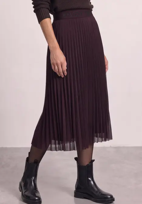 Plissierter Midirock in dunklem Aubergine, schwarze Stiefeletten und feine schwarze Strumpfhose.