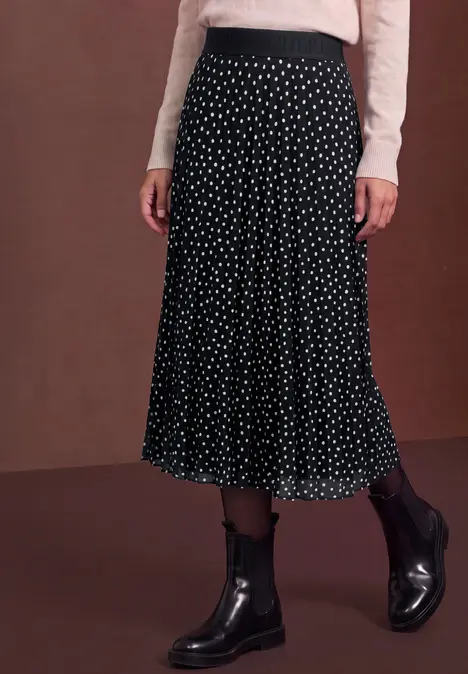 Schwarzer Midirock mit weißen Punkten, kombiniert mit cremefarbenem Oberteil und schwarzen Stiefeletten.