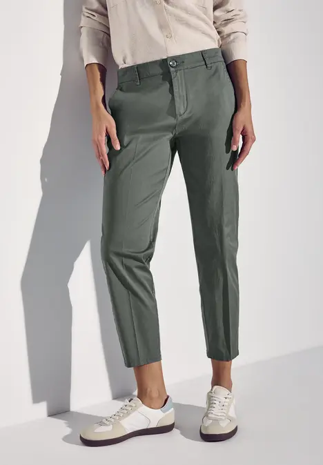 Person trägt grüne Hose, beigene Bluse und weiße Sneaker.