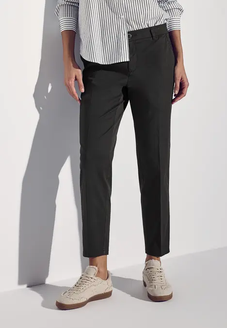 Person trägt schwarze Hose, gestreiftes Hemd und beige Sneaker.