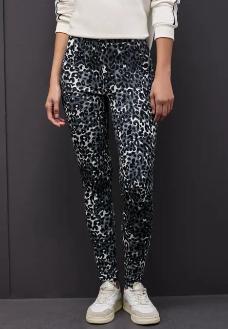 Frau trägt Leggings mit Leopardenmuster, schwarzer Jacke und weißen Sneakers.