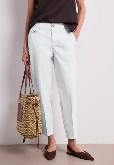 Elegantes Sommeroutfit mit hoch taillierter weißer Hose, lockerem braunen Top, Strohtasche und flachen Slippern.