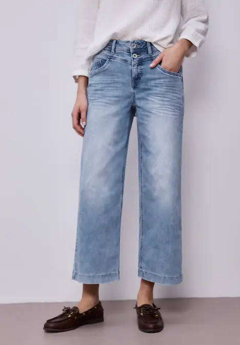 Person trägt weiße Bluse, weite hellblaue Jeans und braune Loafer.