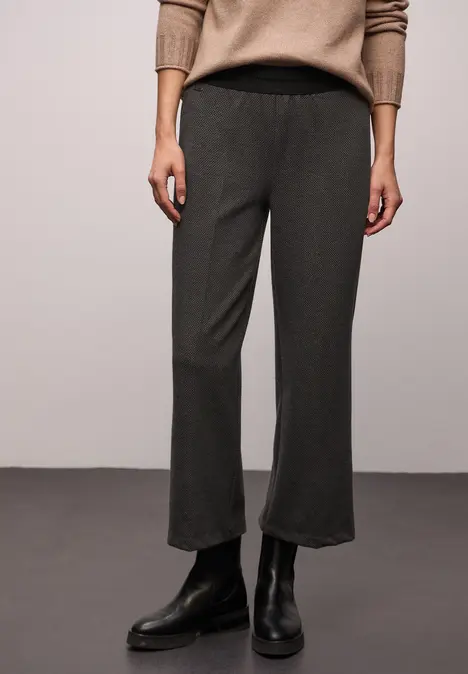 Damenmodel trägt dunkle, gerade geschnittene Hose mit elastischem Bund und schwarze Stiefeletten.