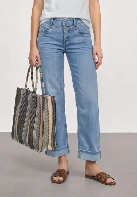 Frau mit umgeschlagenen blauen Jeans, braunen Sandalen und einer gestreiften Einkaufstasche.