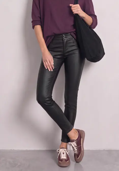 Frau in violettem Shirt, schwarzen Lederleggings und braunen Sneakern, lässig mit Shopper.