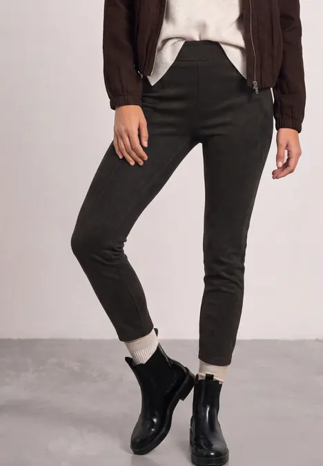 Enge olivgrüne Hose, weiße Socken und schwarze Lederstiefeletten kombiniert mit braunem Blouson.