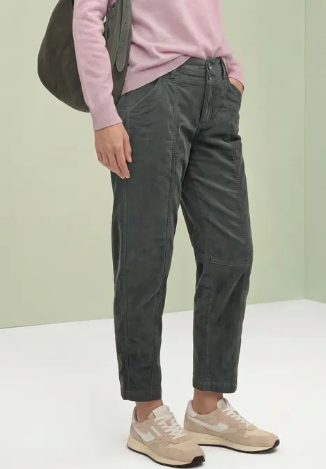 Person trägt pinken Pullover, dunkelgraue Cordhose, beige Sneaker und graue Schultertasche.