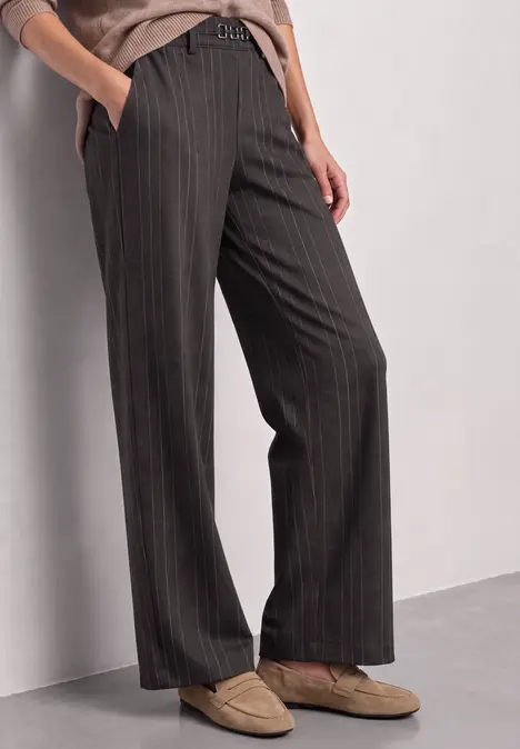 Frau trägt dunkelgraue Nadelstreifen-Hose mit weitem Bein und hellbeigen Loafers.
