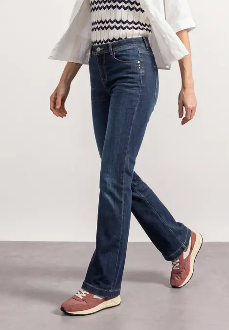 Person in blauen Jeans und rot-beigen Sneakern geht.