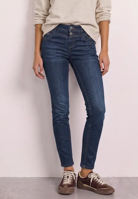 Person trägt hoch geschnittene, dunkelblaue Skinny-Jeans mit Knopfleiste und braune Sneaker.