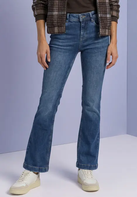 Person trägt dunkelblaue Schlagjeans, weiße Sneaker, schwarzes Top und karierte Jacke.