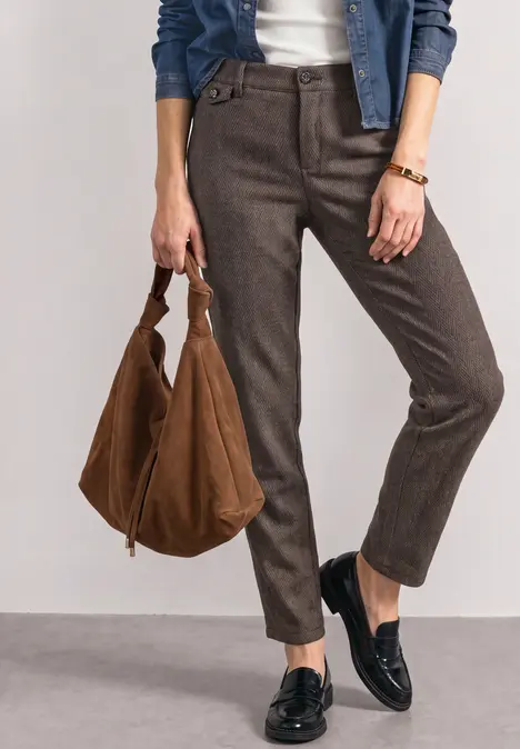 Frau in braunen Hosen, schwarzen Loafers und mit großer brauner Tasche.