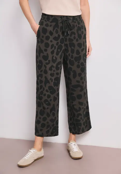 Schwarze, weit geschnittene Hose mit Leopardenmuster, elastischem Bund und Taschen, dazu helle Sneaker.