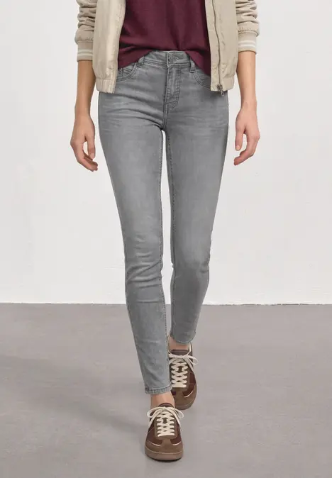 Person trägt graue Skinny Jeans und braune Sneaker vor hellem Hintergrund.