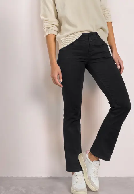 Person in schwarzer Jeans und weißen Sneakers, Oberteil in hellem Farbton.