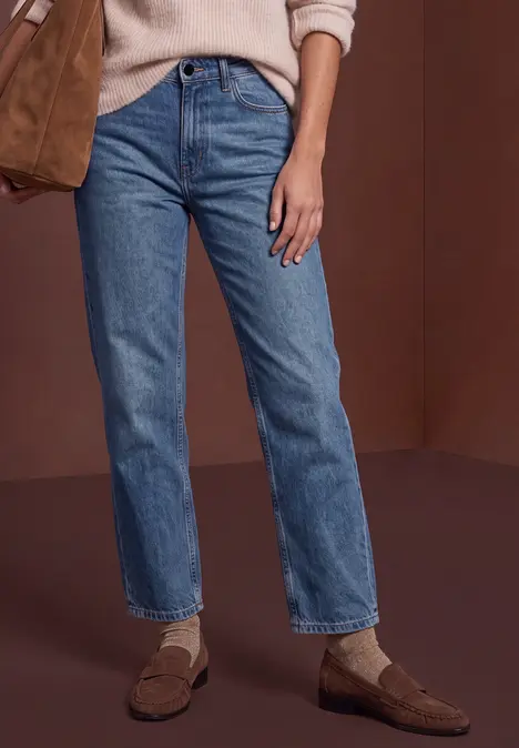 Une personne porte un jean droit bleu, des chaussettes blanches et des mocassins marron.