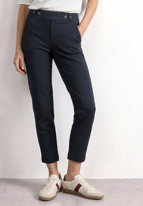Feminine, knöchellange, dunkelblaue, schmale Stoffhose kombiniert mit weißen Sneakern.