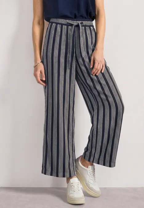 Graue, hochtaillierte, weit geschnittene Hose mit schwarzen Streifen und Bindegürtel, kombiniert mit weißen Sneakern.