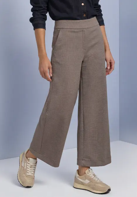 Model trägt weite, knöchellange, beige Stoffhose mit Seitennahttaschen und beigefarbenen Sneakers.