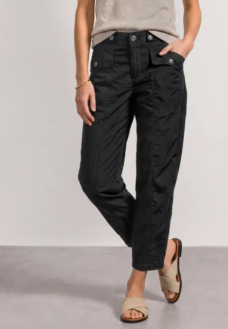 Frau trägt schwarze, knöchellange Hose mit hoher Taille und Schnappverschlüssen, kombiniert mit Sandalen.