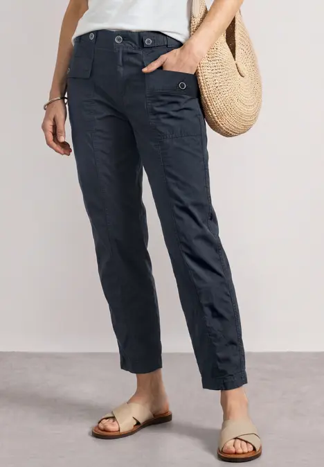 Dunkelblaue, knöchellange Cargohose mit Taschen, kombiniert mit Sandalen und Strohtasche.
