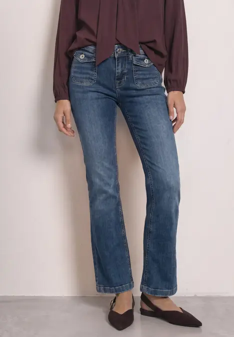 Frau in dunkelblauen, geraden Jeans und spitzen Ballerinas, kombiniert mit einer weiten, dunkelroten Bluse.