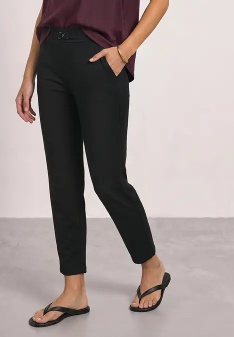 Schlanke, knöchellange schwarze Hose mit seitlichen Taschen, kombiniert mit schwarzen Flip-Flops.
