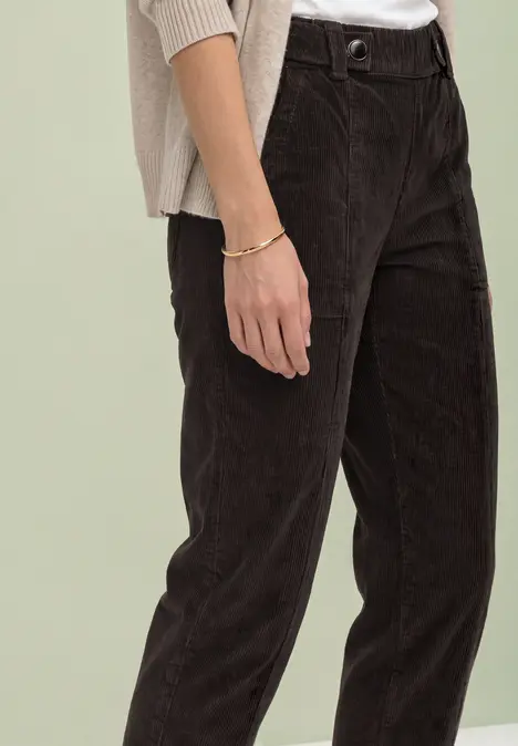 Gedeeltelijk beeld van persoon in donkerbruine corduroy broek, licht topje en zichtbaar armbandje.