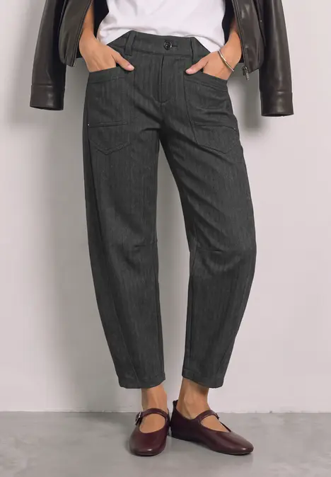 Damen in grauen Nadelstreifen-Hosen, weißem Shirt und dunkelroten Mary-Jane-Schuhen.