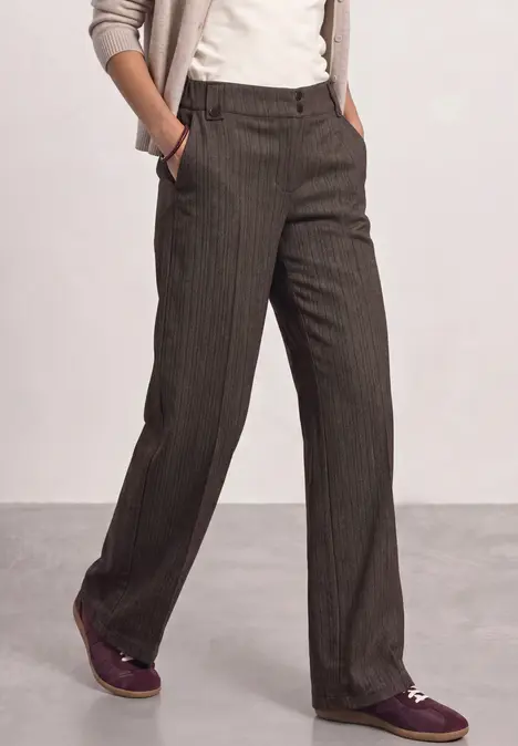 Person trägt graue, gestreifte Hose, weißes Shirt, beigefarbener Cardigan und lila Schuhe.