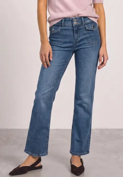 Frau in blauen, gerade geschnittenen Jeans und schwarzen Ballerinas, nur Unterkörper sichtbar.