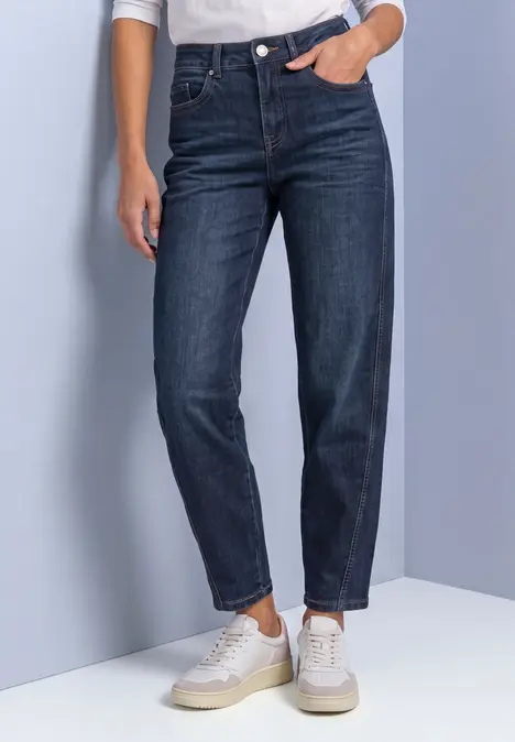 Hoch geschnittene, dunkelblaue Damenjeans mit schmaler Passform, leicht gekrempelt, kombiniert mit weißen Sneakern.