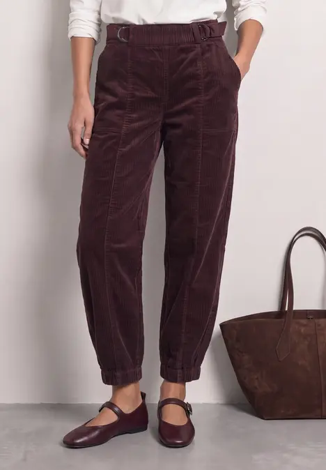 Dunkelrote Cordhose mit hohem Bund, lockerer Passform und elastischen Umschlagsäumen, kombiniert mit Mary-Jane-Schuhen.