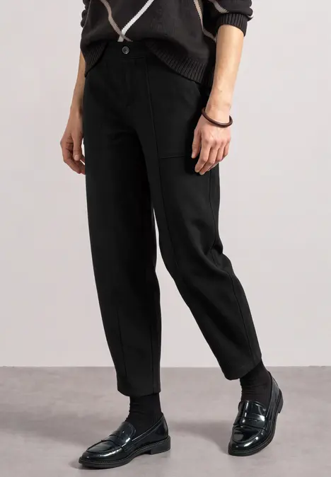 Eine Person trägt schwarze Stoffhose und glänzende schwarze Loafers auf grauem Boden.