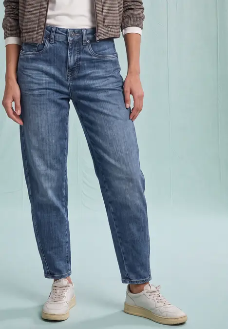 Eine Person trägt blaue Jeans und weiße Sneaker vor hellem Hintergrund.