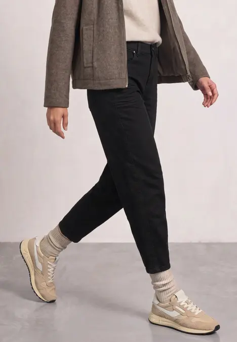 Eine Person in schwarzer Hose, grauen Socken und beigen Sneakers beim Gehen.