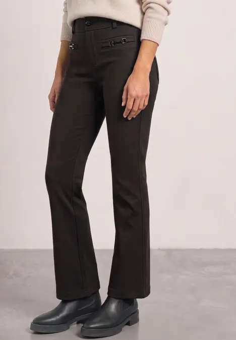 Pantalon brun foncé à coupe droite légèrement évasée, porté avec des bottines noires.