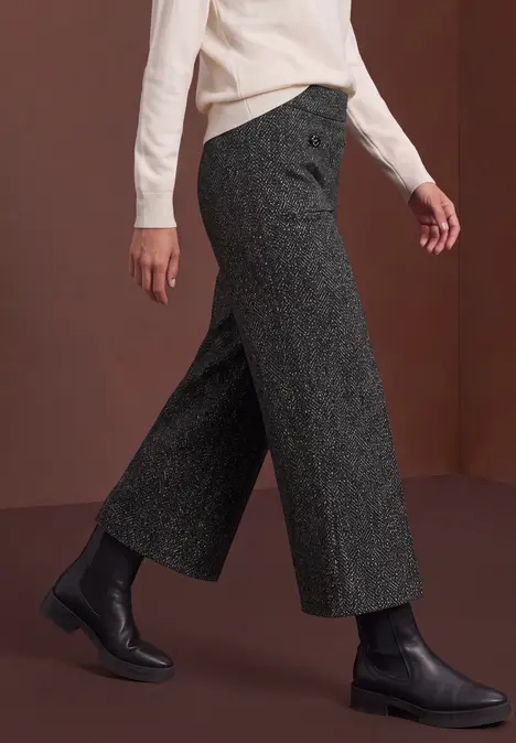 Seitenansicht: Weite graue Wollhose mit hohem Bund, schwarze Stiefeletten und weißes Oberteil.