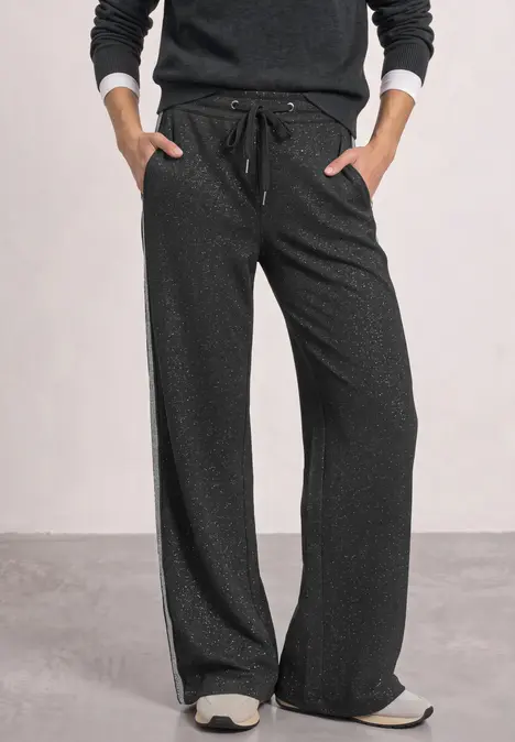 Pantalon ample noir à cordon, bandes latérales, porté avec des baskets blanches.