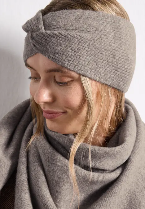 Junge Frau im Profil mit grauem, gestricktem Stirnband und passendem Schal, dezent lächelnd.