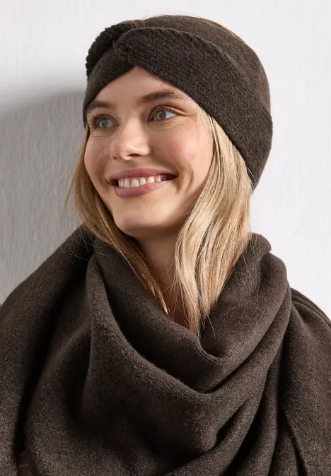 Frau mit braunem Turban-Stirnband und passendem Schal, lächelnd, blondes Haar, vor hellem Hintergrund