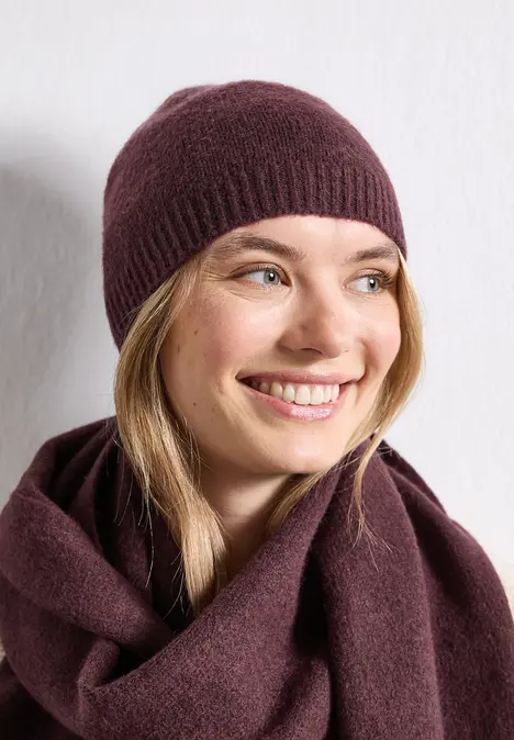 Femme souriante portant un bonnet en maille bordeaux et une écharpe assortie, fond blanc.