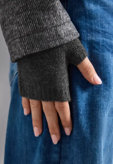 Hand in grauem, fingerlosen Handschuh ruht auf blauen Jeans.